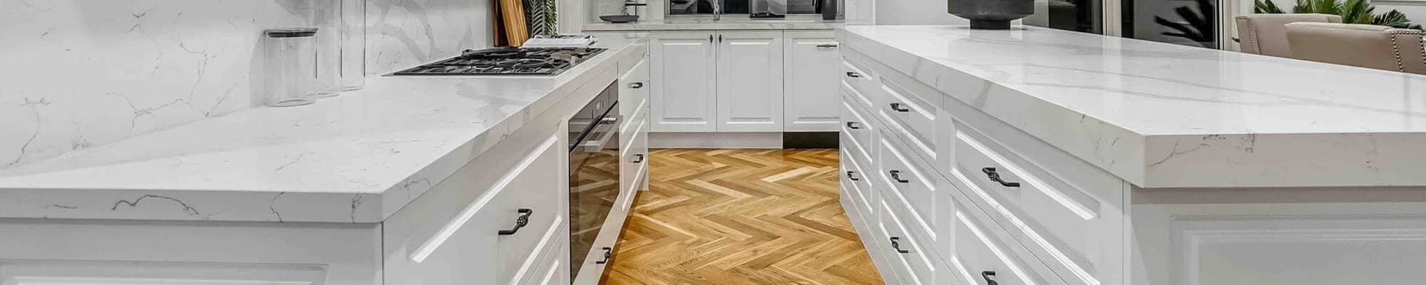 Herringbone patterned hardwood floors in a kitchen with white cabinets